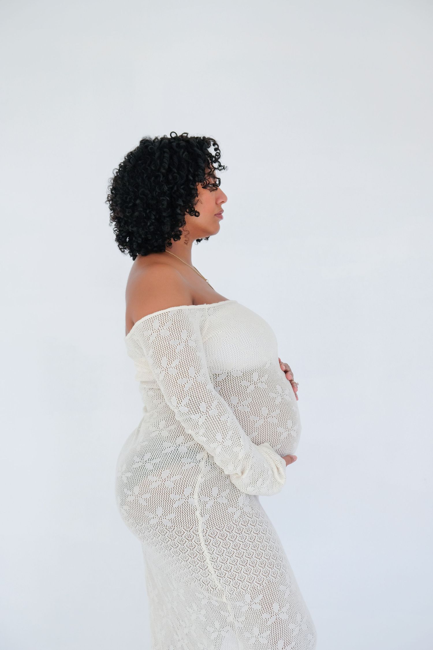 A figure wrapped in a white lace dress poses against a light background in a series of artistic maternity portraits.