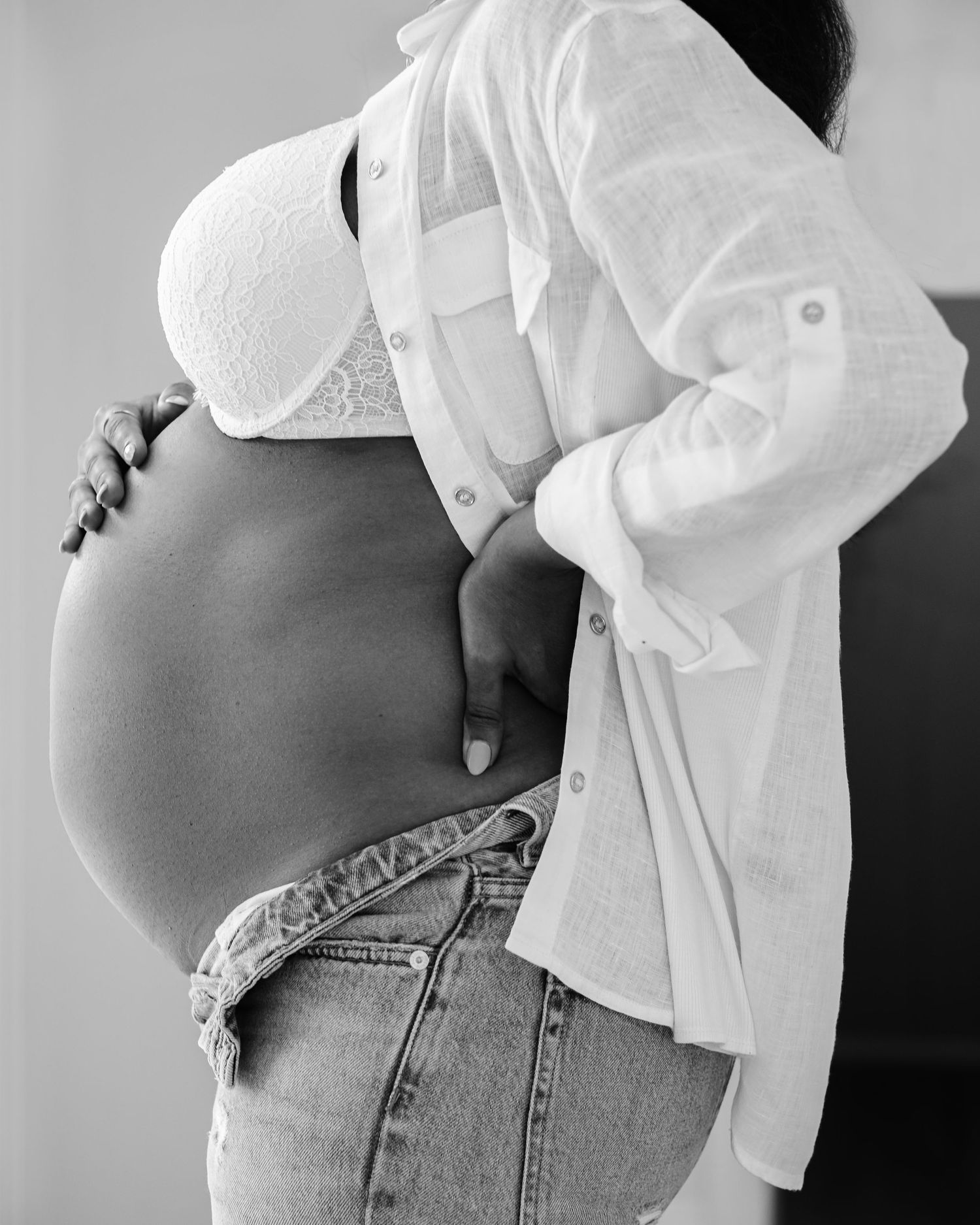 A black and white photo series showing a pregnant belly with a white button-down shirt and blue jeans in different poses.