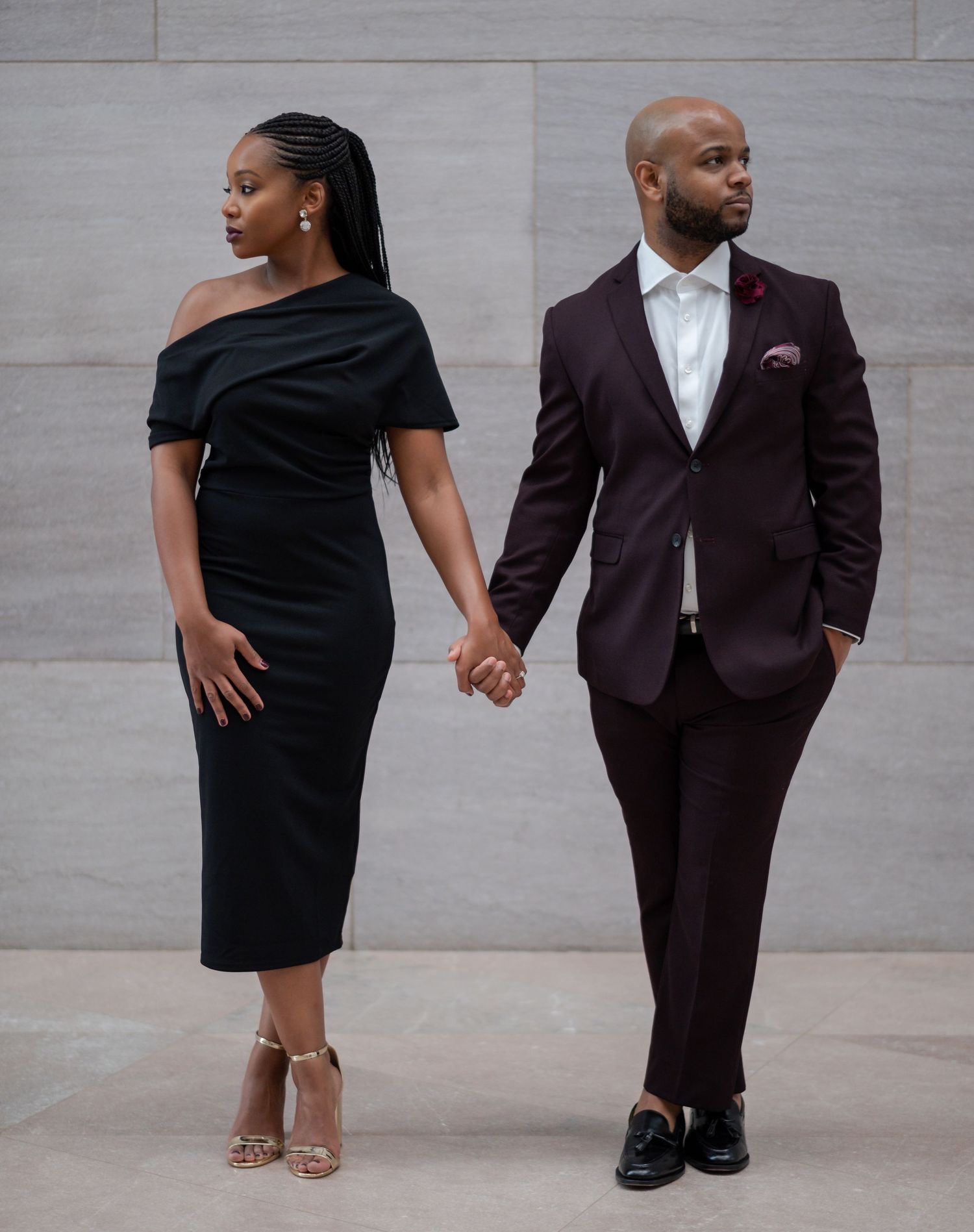 Elegant couple in evening wear striking poses against a modern concrete backdrop.