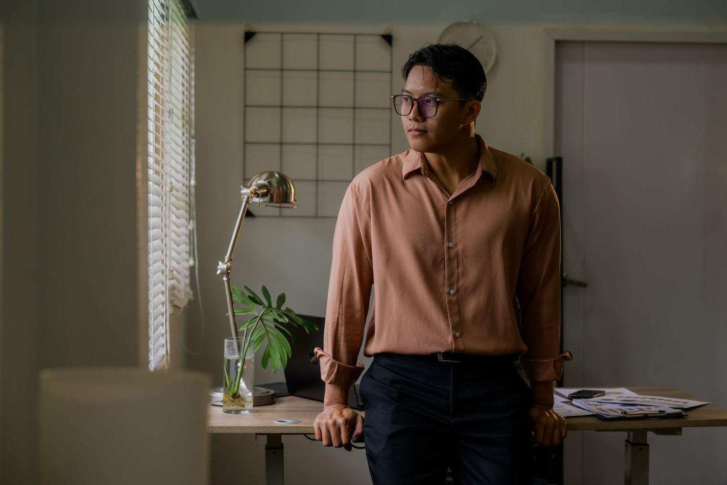 Person in peach colored shirt sitting by window with indoor plants.
