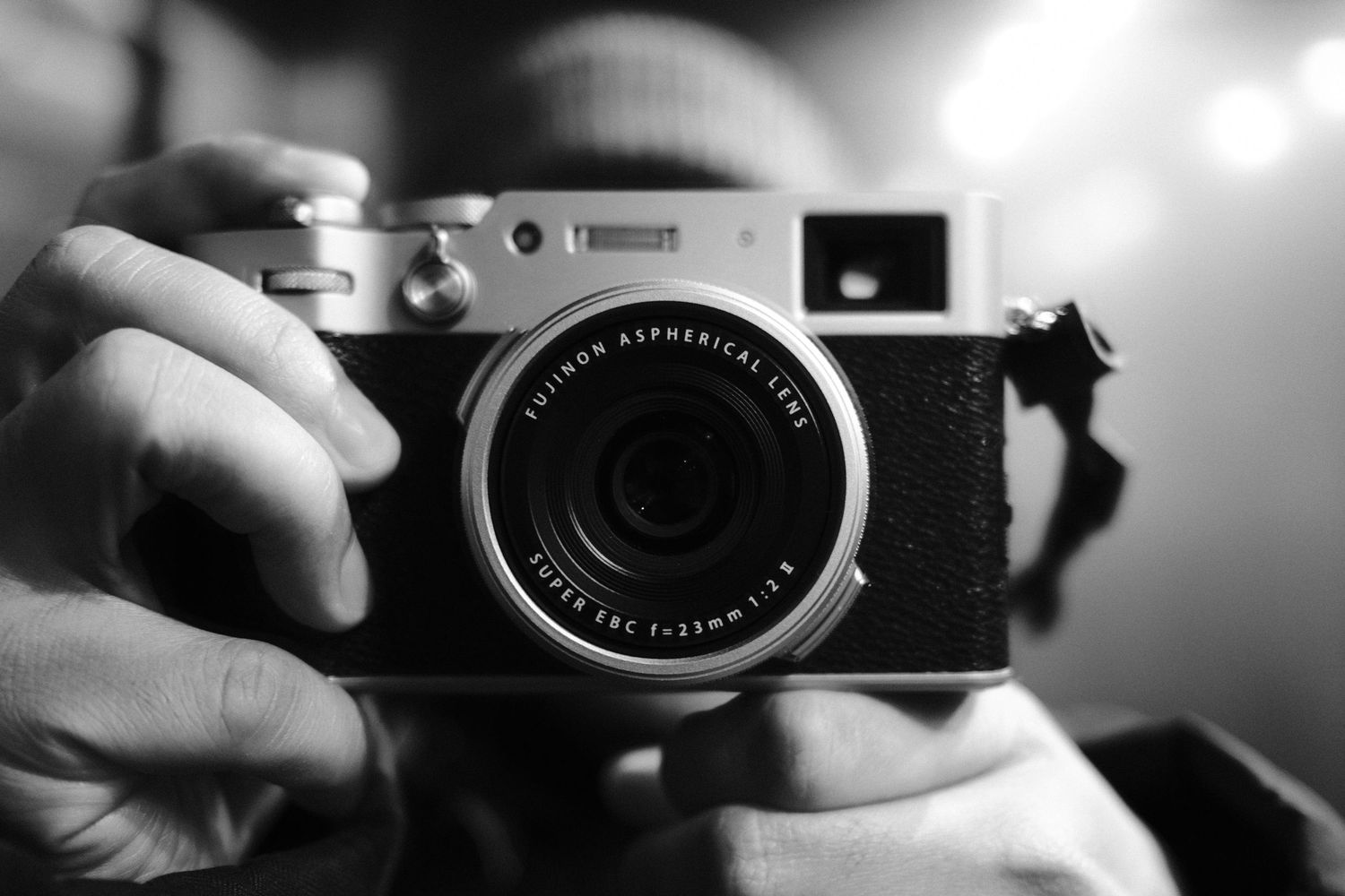 Detailed view of someone holding a digital camera with a prominent lens in monochrome.