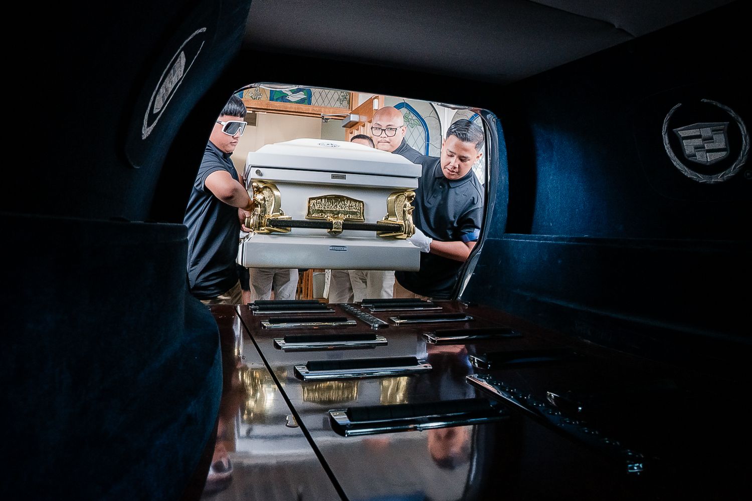 Guam funeral photographer capturing family members carefully loading a white and gold casket into a hearse.