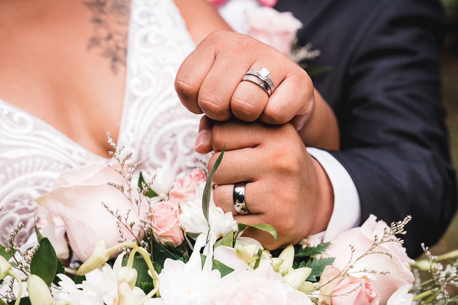 Guam wedding photographer capturing newlyweds interlocking fingers showing wedding bands over a bouquet of pink and white flowers.