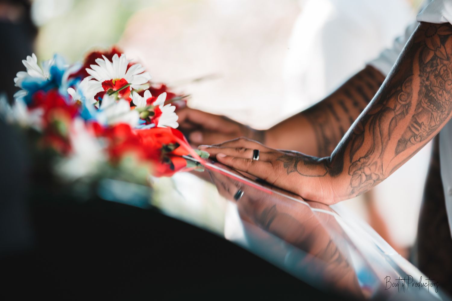 Guam funeral photographer capturing tattooed hands holding red, white, and blue flowers at a wedding ceremony outdoors.