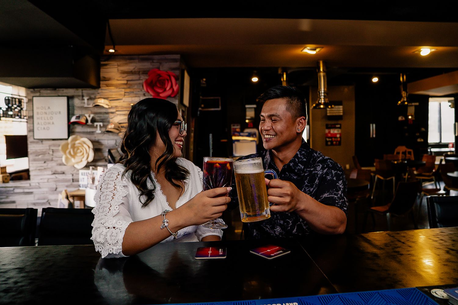 Couple laughing and toasting with beer glasses at a bar, enjoying a fun date night together.