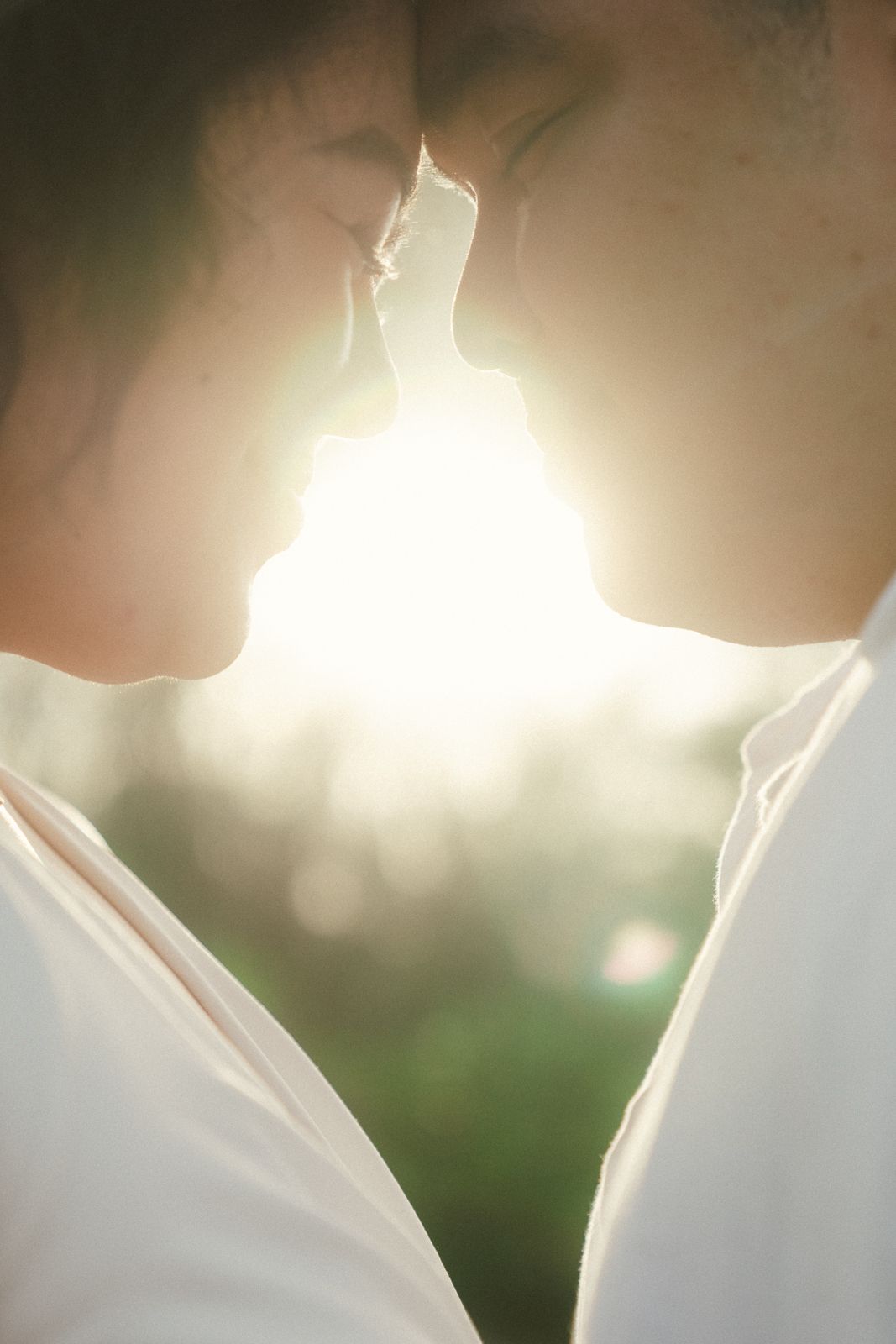 Romantic couple sharing a tender moment face to face, backlit by warm golden sunlight outdoors.