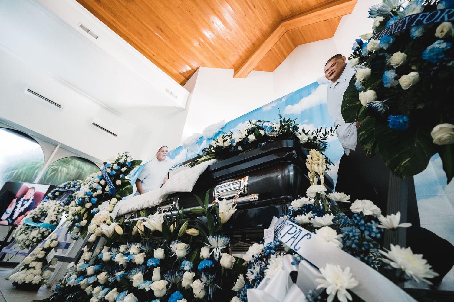 Guam funeral photographer capturing an elegant funeral casket surrounded by blue and white floral arrangements inside a chapel.