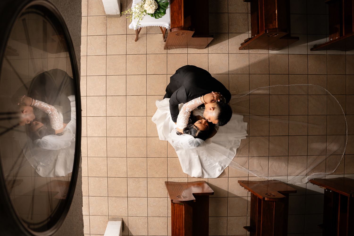 Guam wedding photographer capturing an aerial view of bride and groom embracing on tiled church floor with veil spread out.