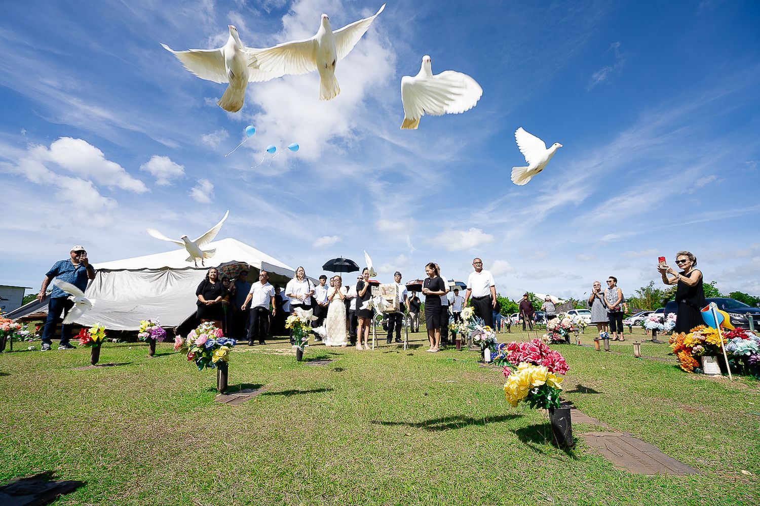 Guam funeral photographer capturing family releasing white doves into a bright blue sky during an outdoor ceremony at a memorial garden.