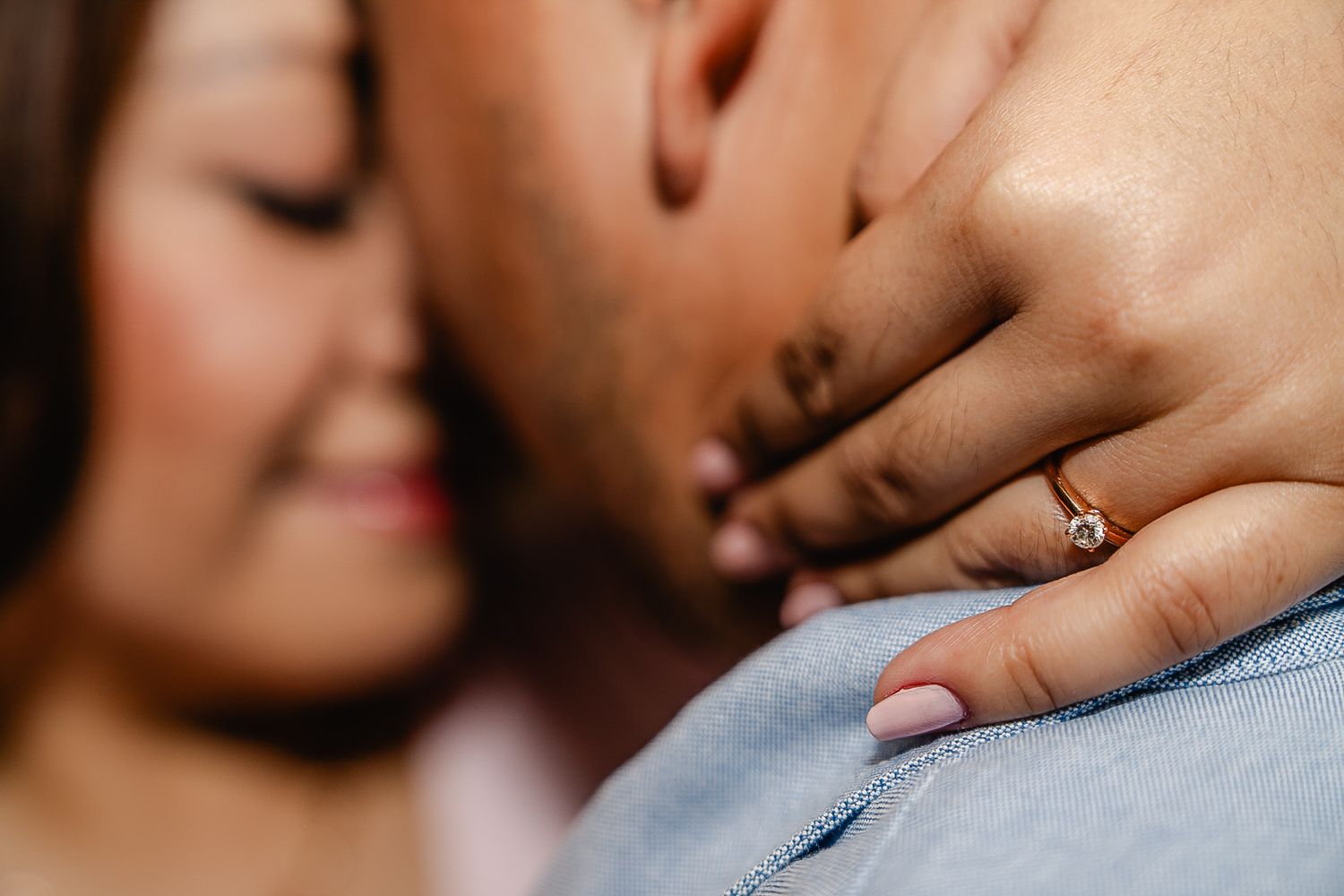 Close-up of a couple embracing, woman wearing a diamond engagement ring on her hand resting on man's chest.