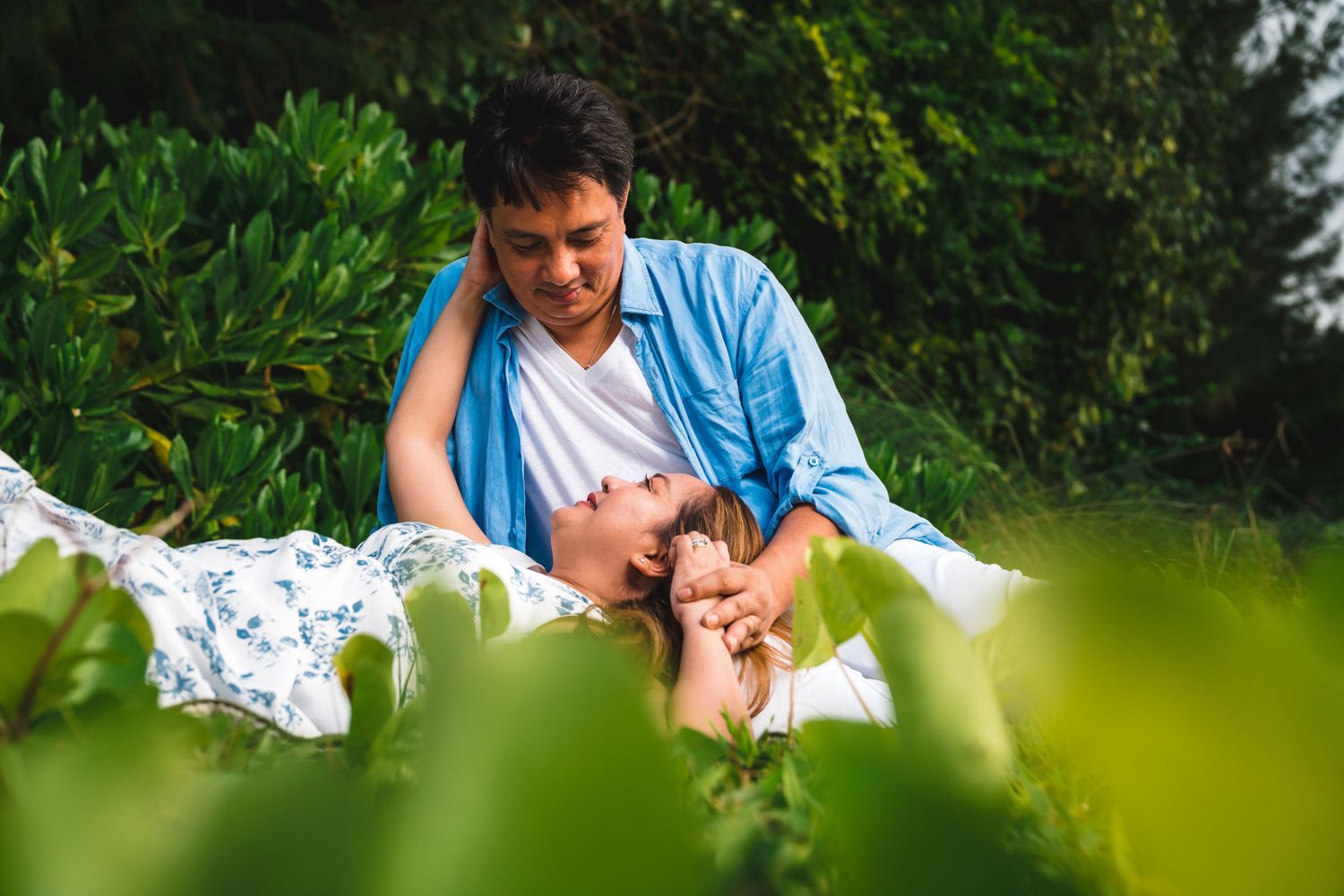 Romantic couple relaxing together in lush green garden, woman lying in man's lap outdoors.