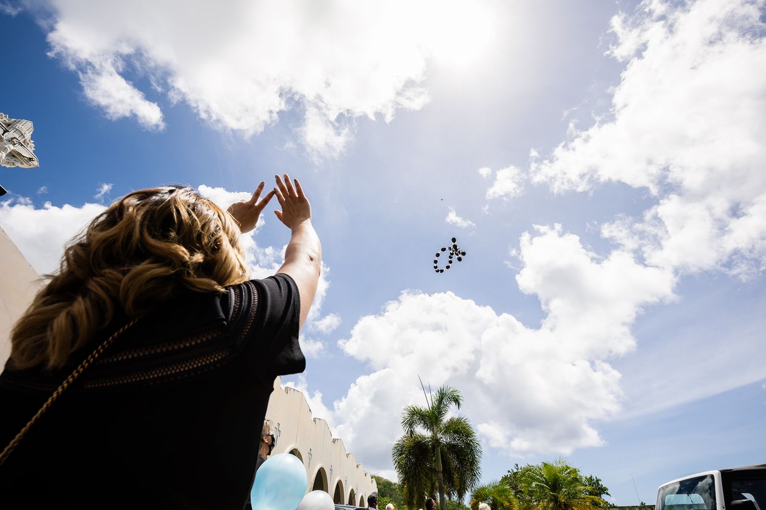 Guam funeral photographer capturing a woman releasing a butterfly into the sky during an outdoor memorial service on a sunny day.