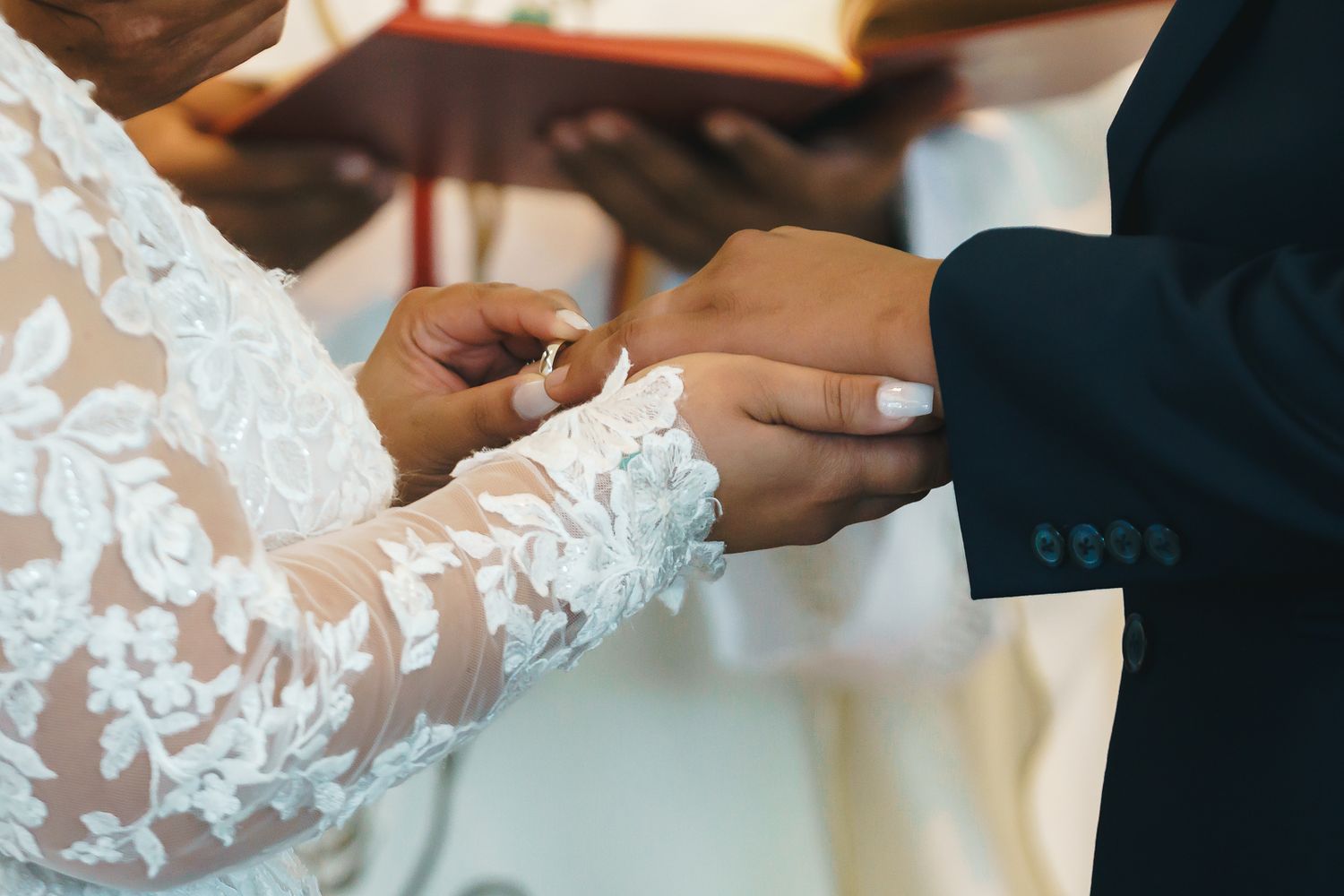 Guam wedding photographer capturing a bride in lace gown places wedding ring on groom's finger during ceremony.