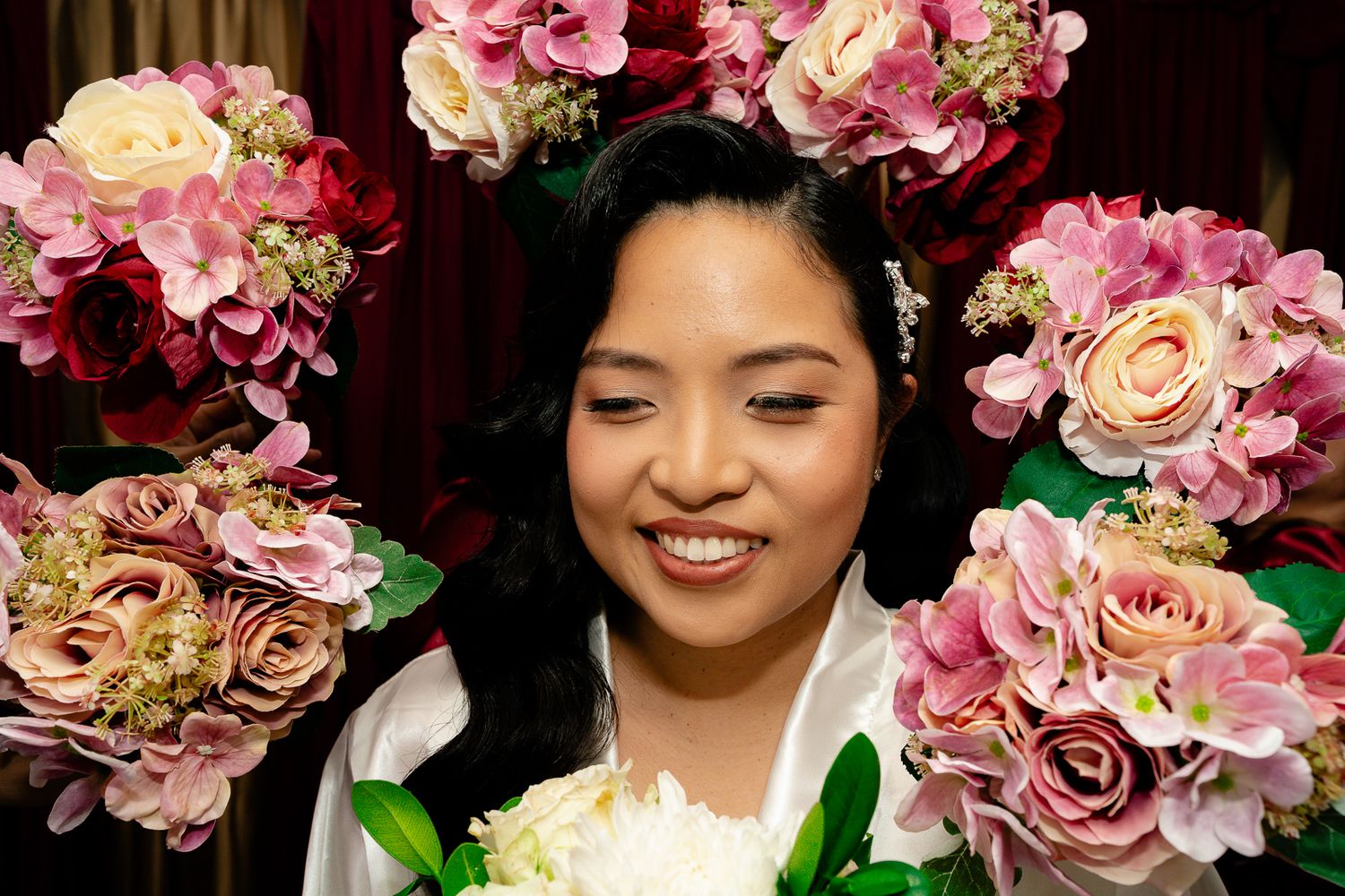 Guam wedding photographer capturing a smiling bride surrounded by colorful pink, red, and white floral arrangements on her wedding day.