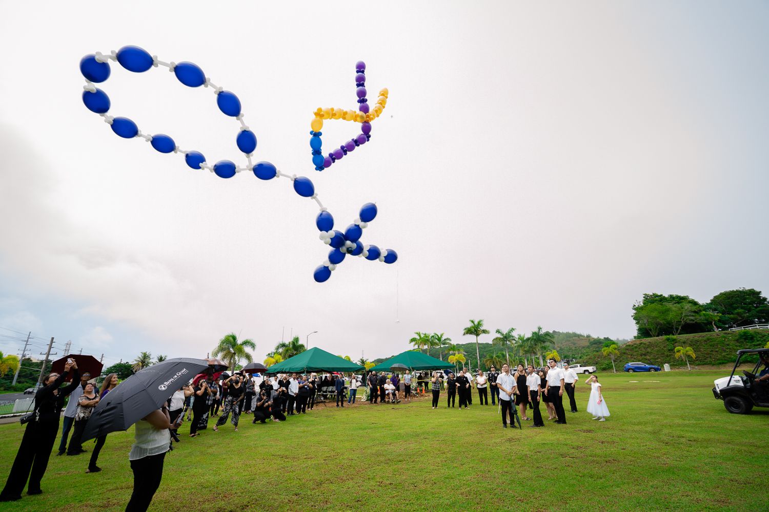 Guam funeral photographer capturing colorful balloons shaped as a cross released into the sky during an outdoor memorial ceremony.