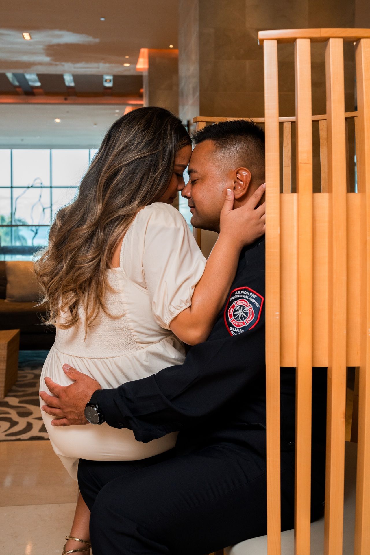 A couple shares an intimate moment, embracing near wooden decor in an elegant hotel lobby setting.