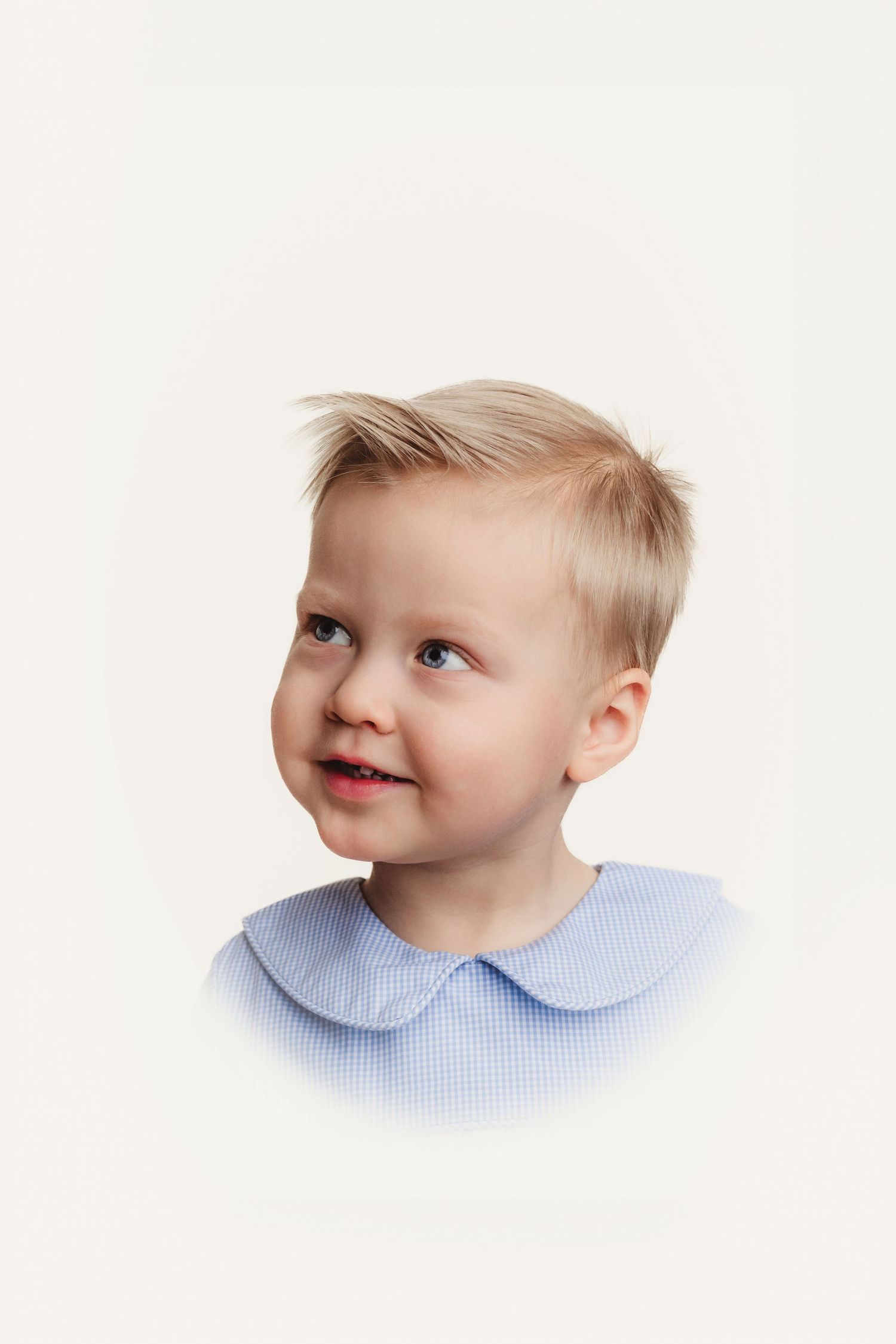 Portrait of toddler in light blue peter pan collar shirt against white background.