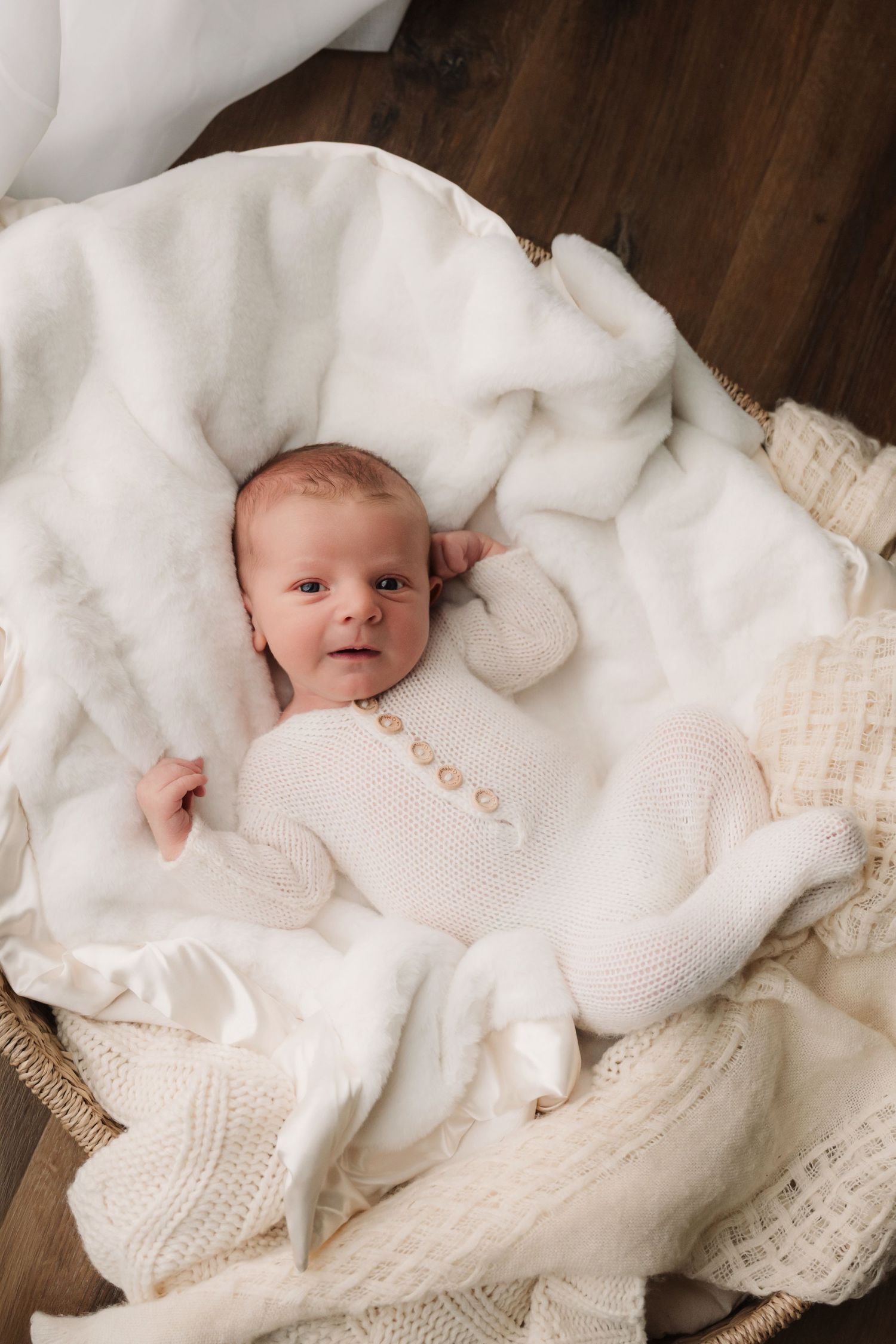 Baby in white knit outfit lying on plush white blankets.
