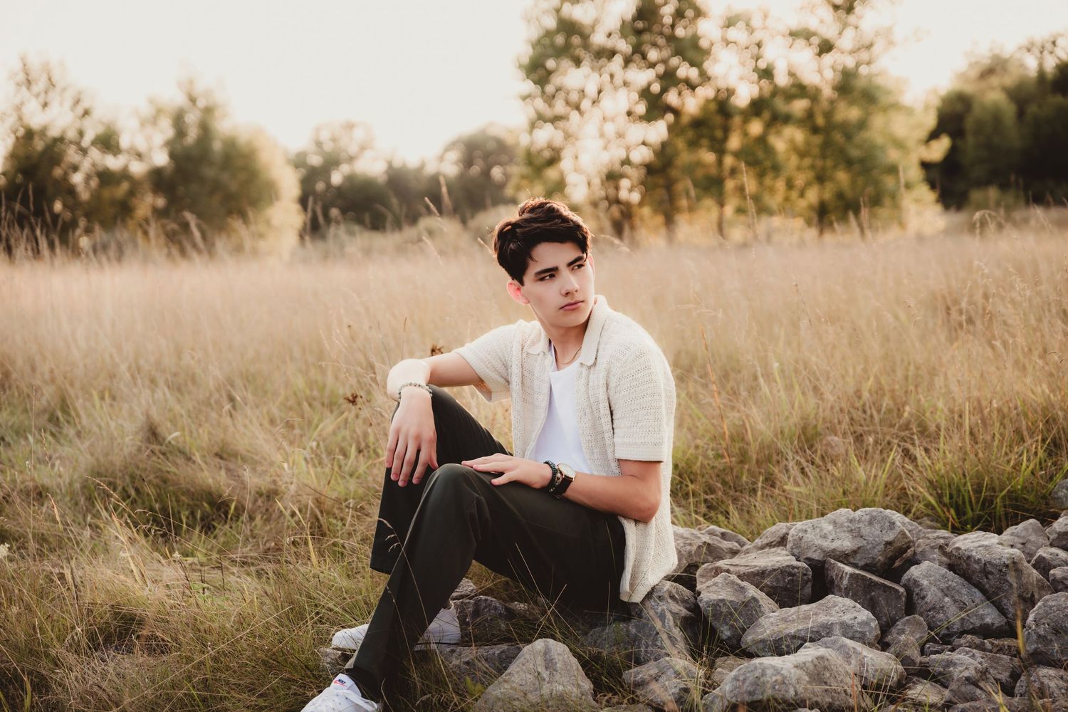 Young person sitting on rocks in field during golden hour sunset.