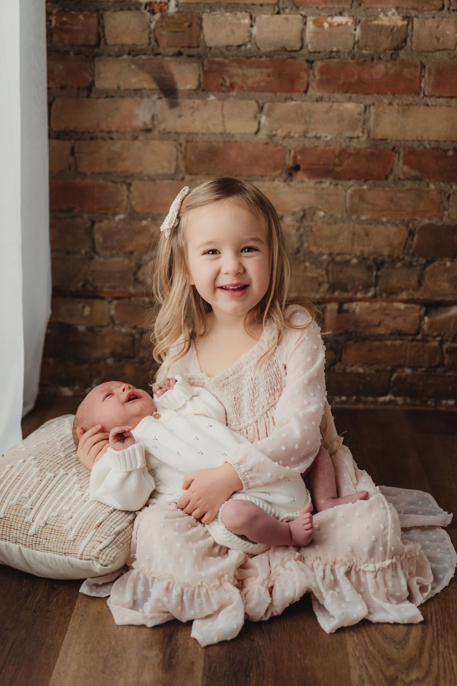 Three connected photos show siblings in vintage-style white lace dresses sitting on a wooden floor against a brick wall.