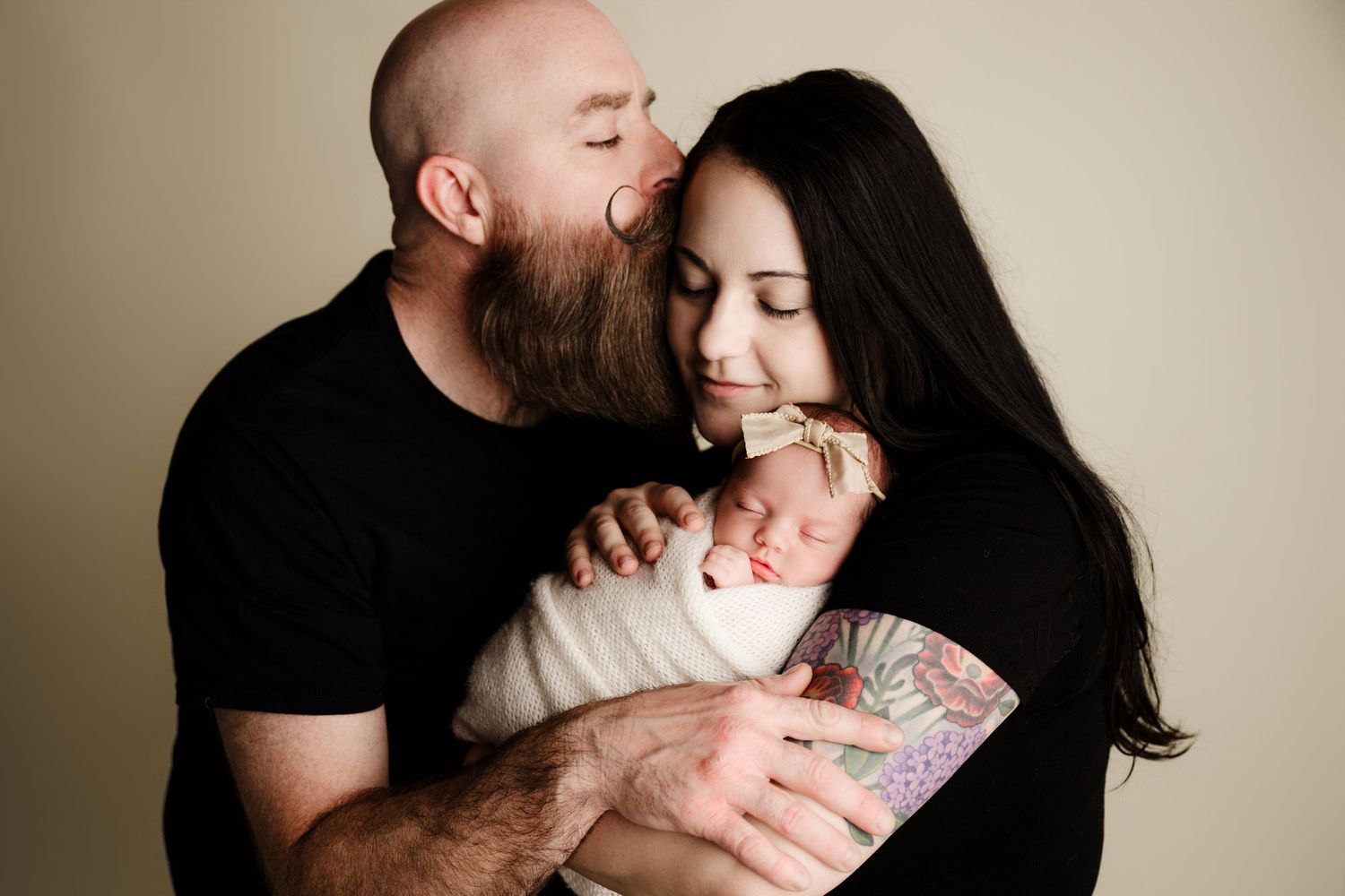 Intimate family portrait in neutral tones showing tender moment with newborn.