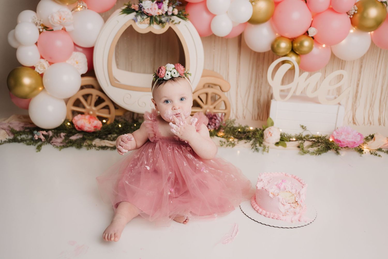 First birthday cake smash setup with pink and gold balloons and floral decorations.