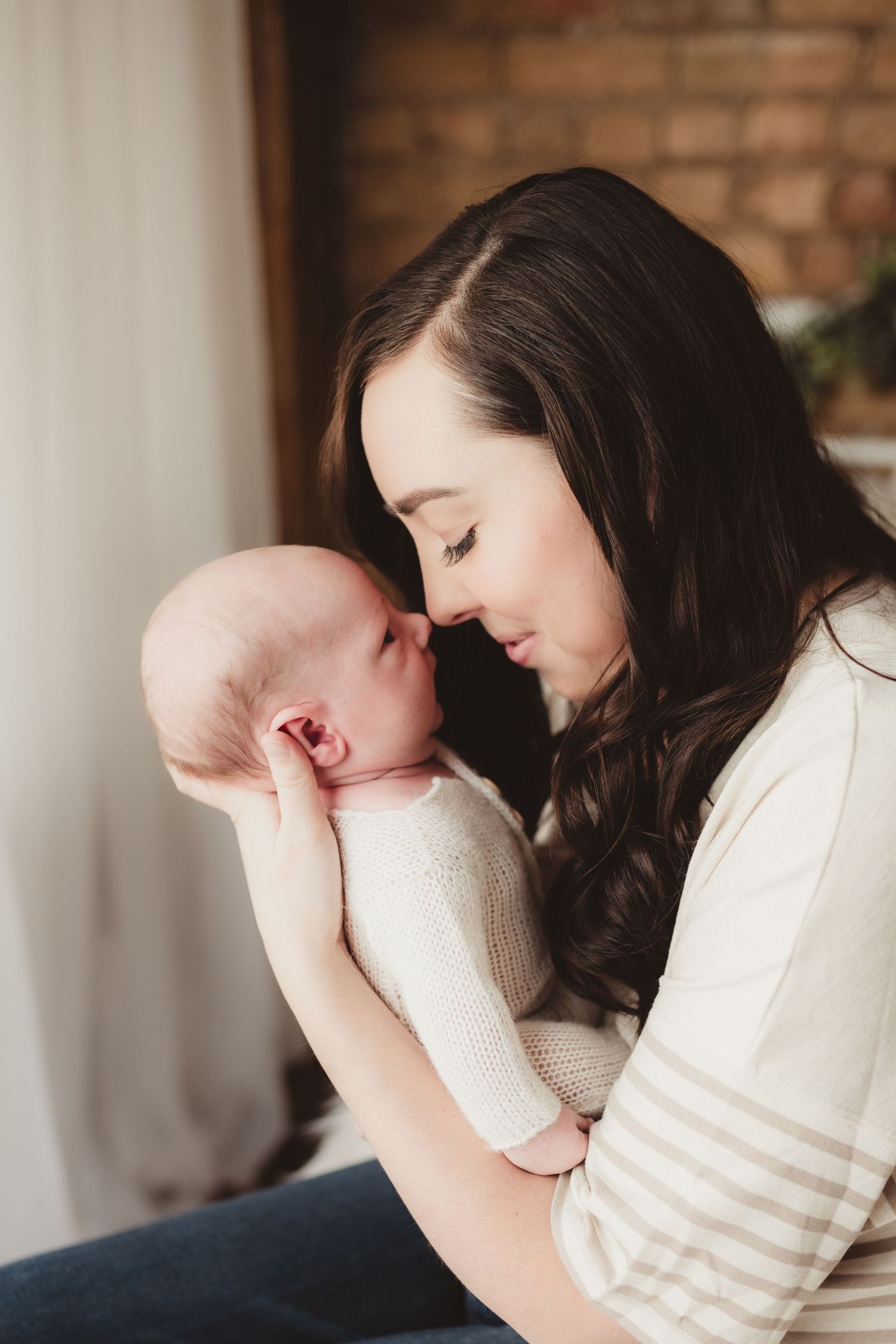 Tender moment between mother and newborn against brick wall background.