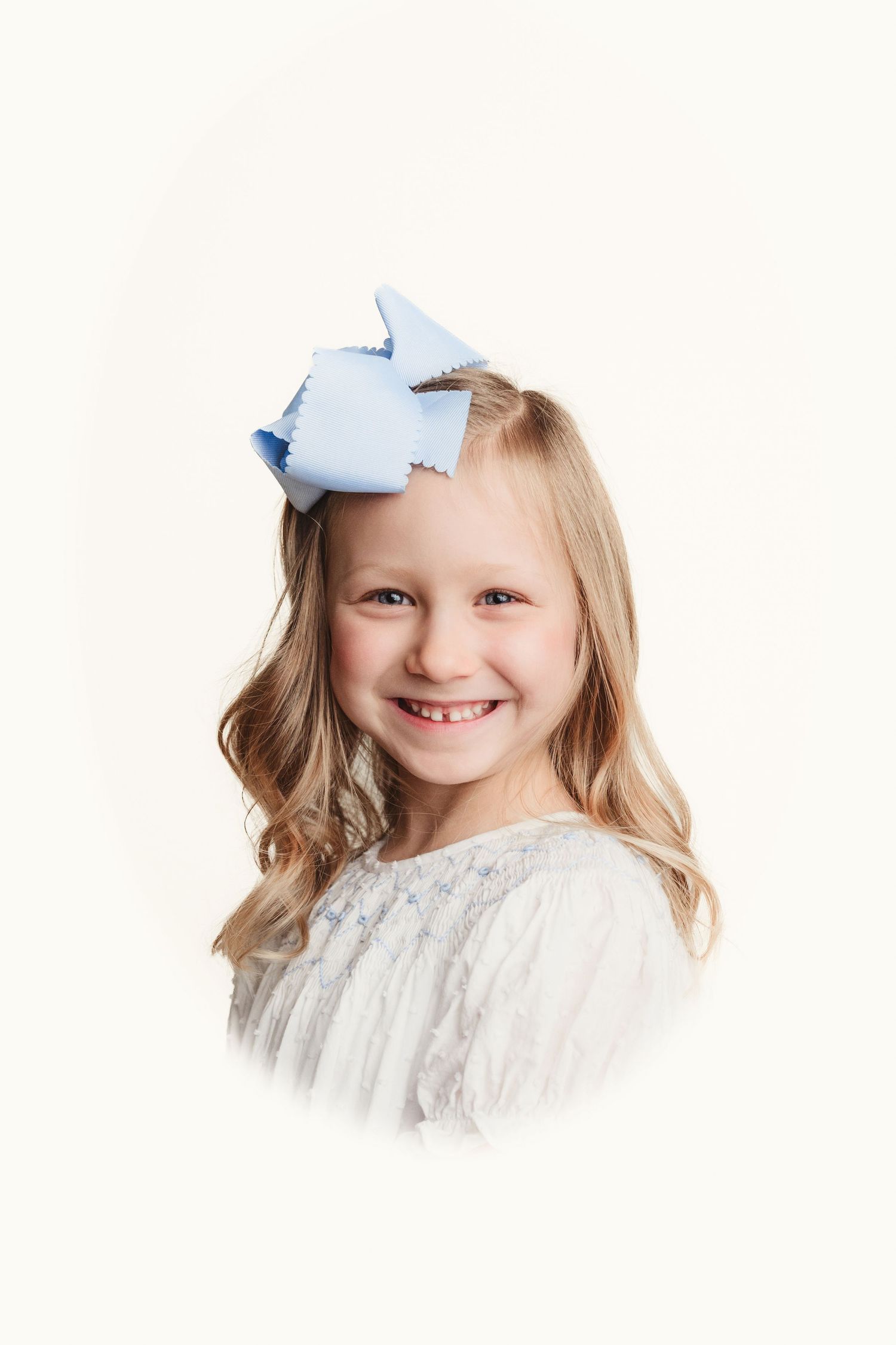 Studio portrait of young blonde child wearing a blue bow and white lace dress against white background.