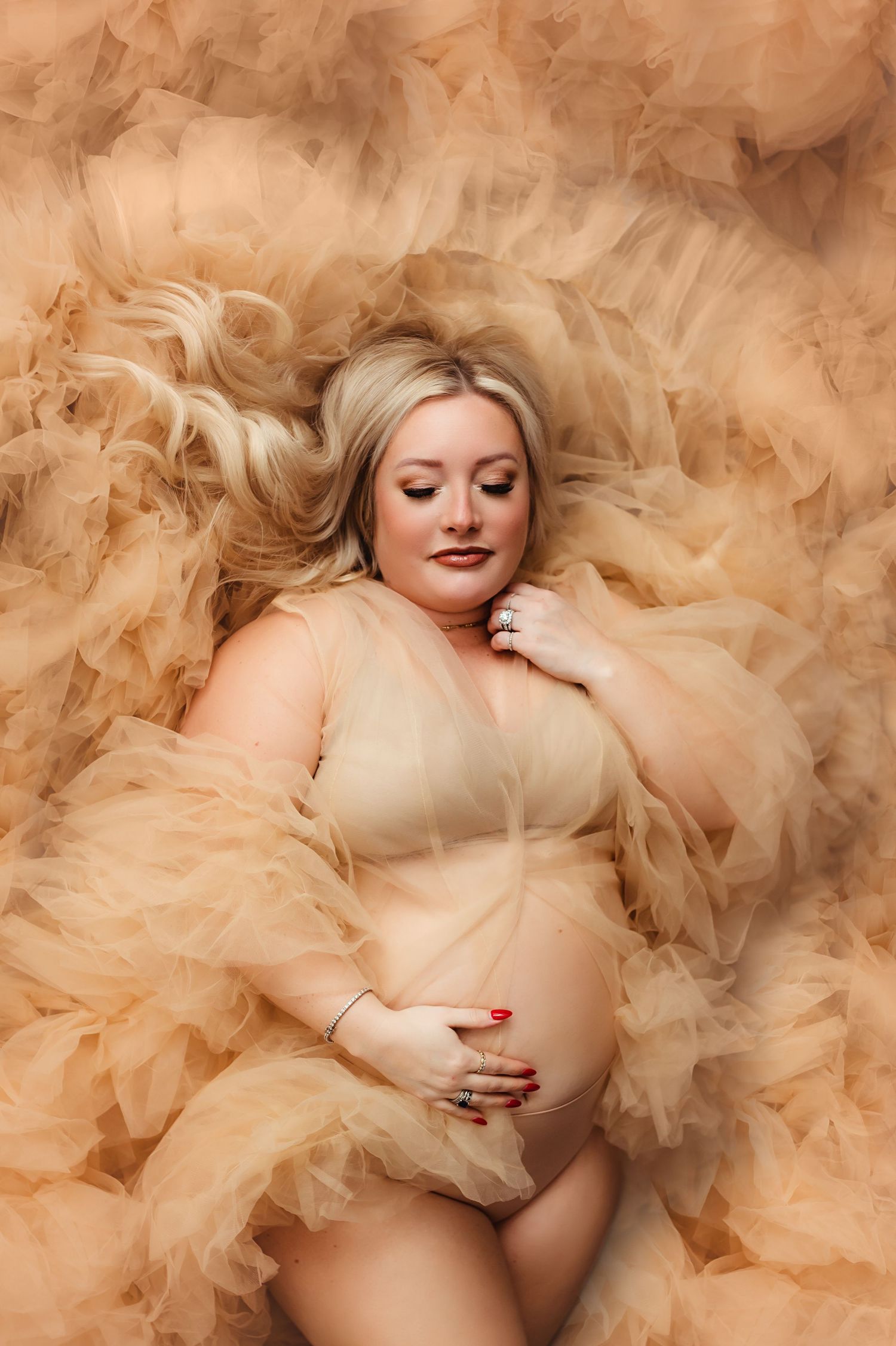 Ethereal maternity photo with flowing peach tulle fabric surrounding expectant mother.
