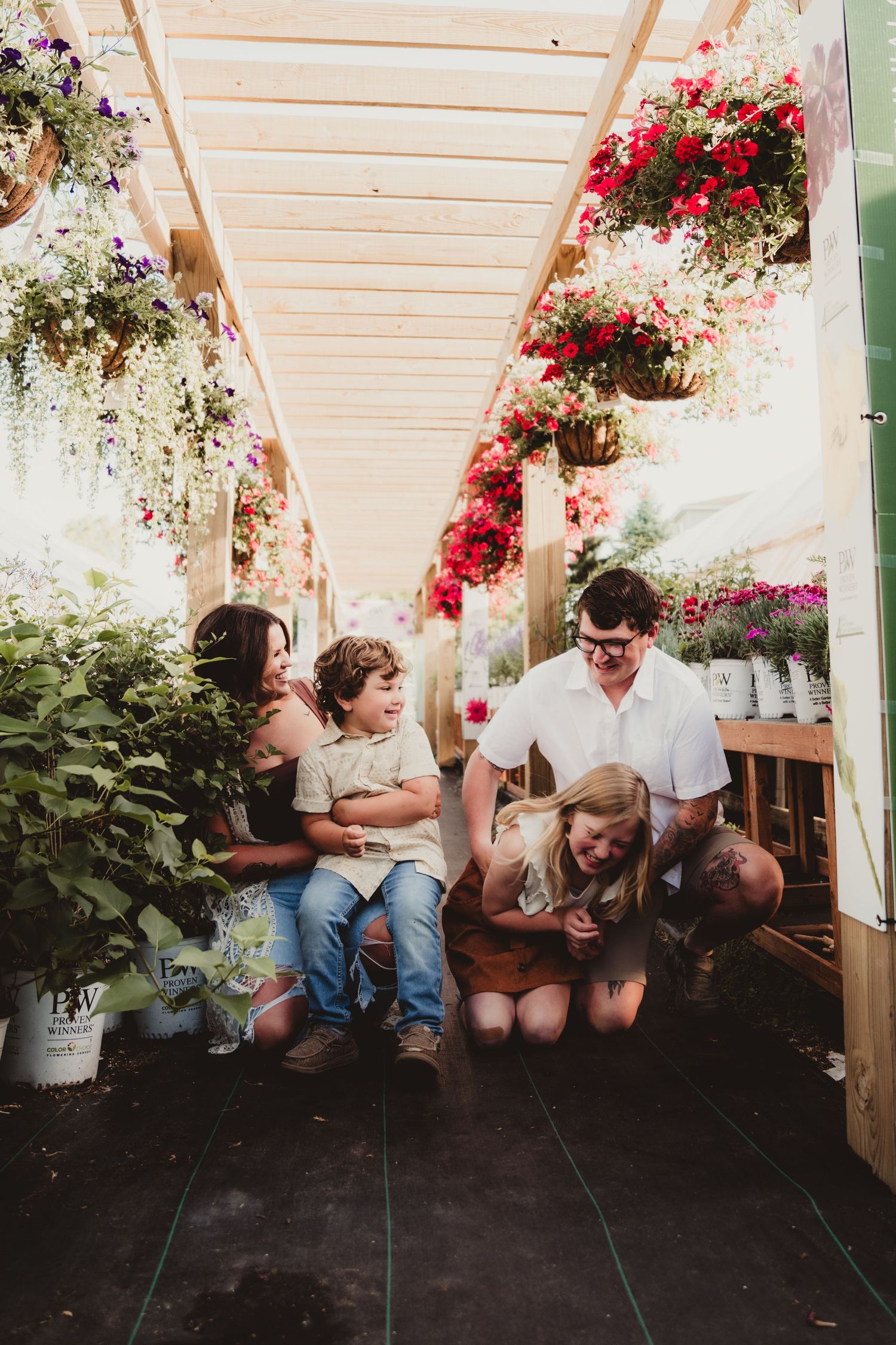 Family moment captured in greenhouse corridor with hanging flower baskets.