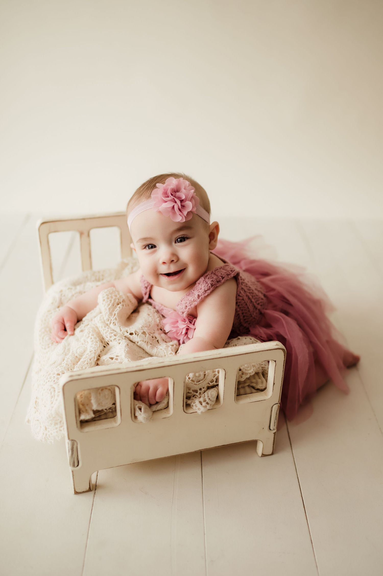 Baby in pink tulle dress sitting in vintage white wooden bed frame.