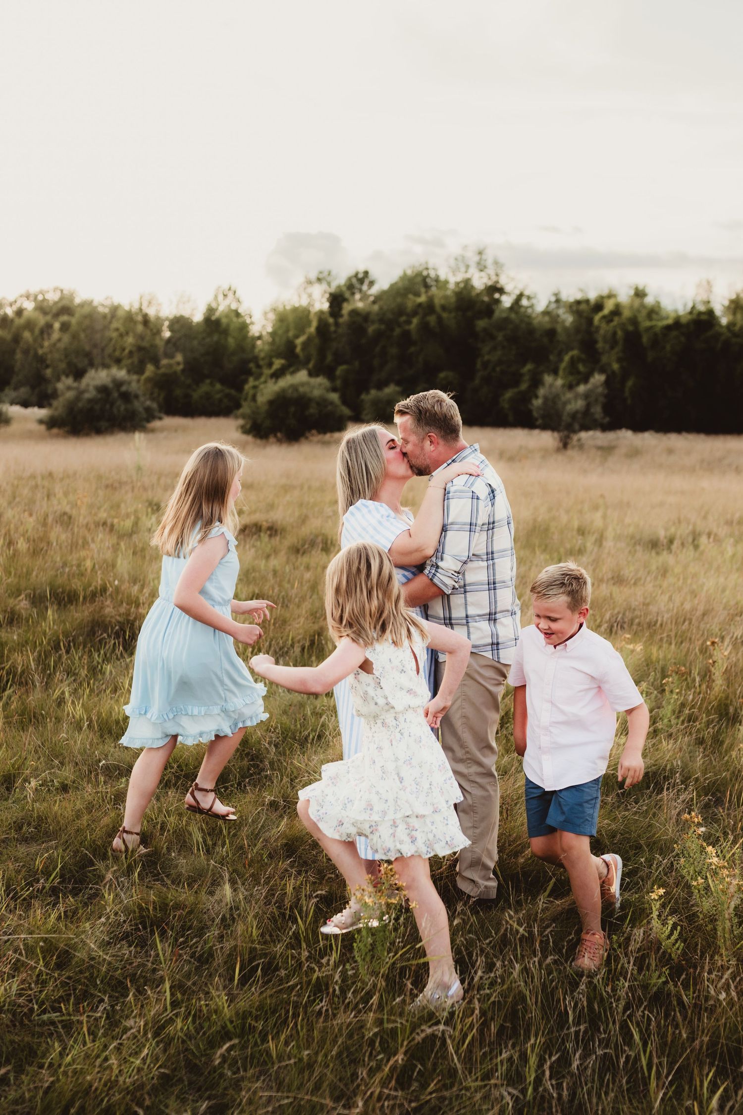 Family playing and dancing together in golden field at sunset.