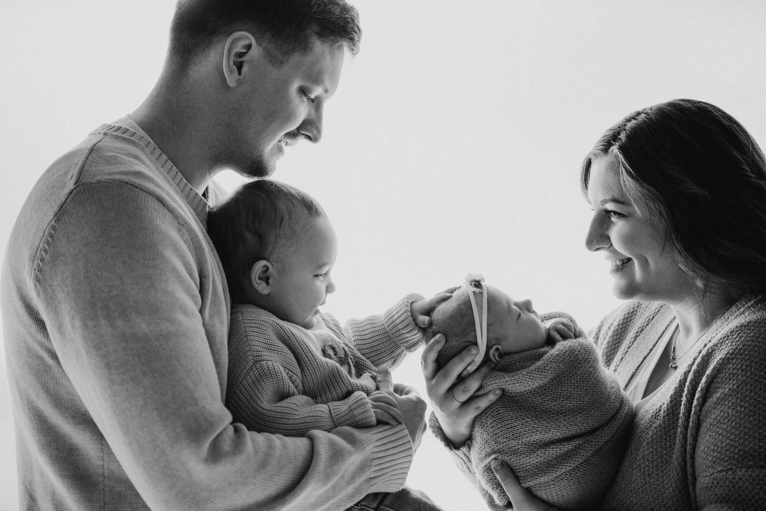 Black and white photo of new parents sharing a tender moment with their newborn baby.