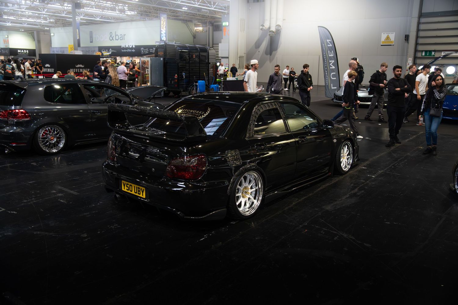 Black modified Mitsubishi Lancer Evolution sedan on display at an indoor car show.