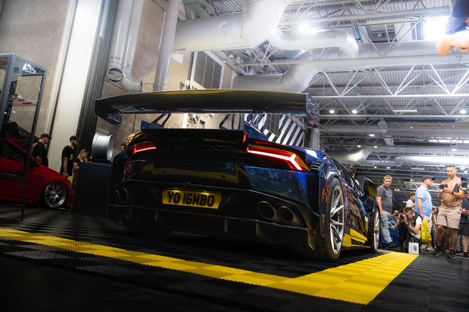 Rear view of a blue Lamborghini with large spoiler and custom plate at car show.