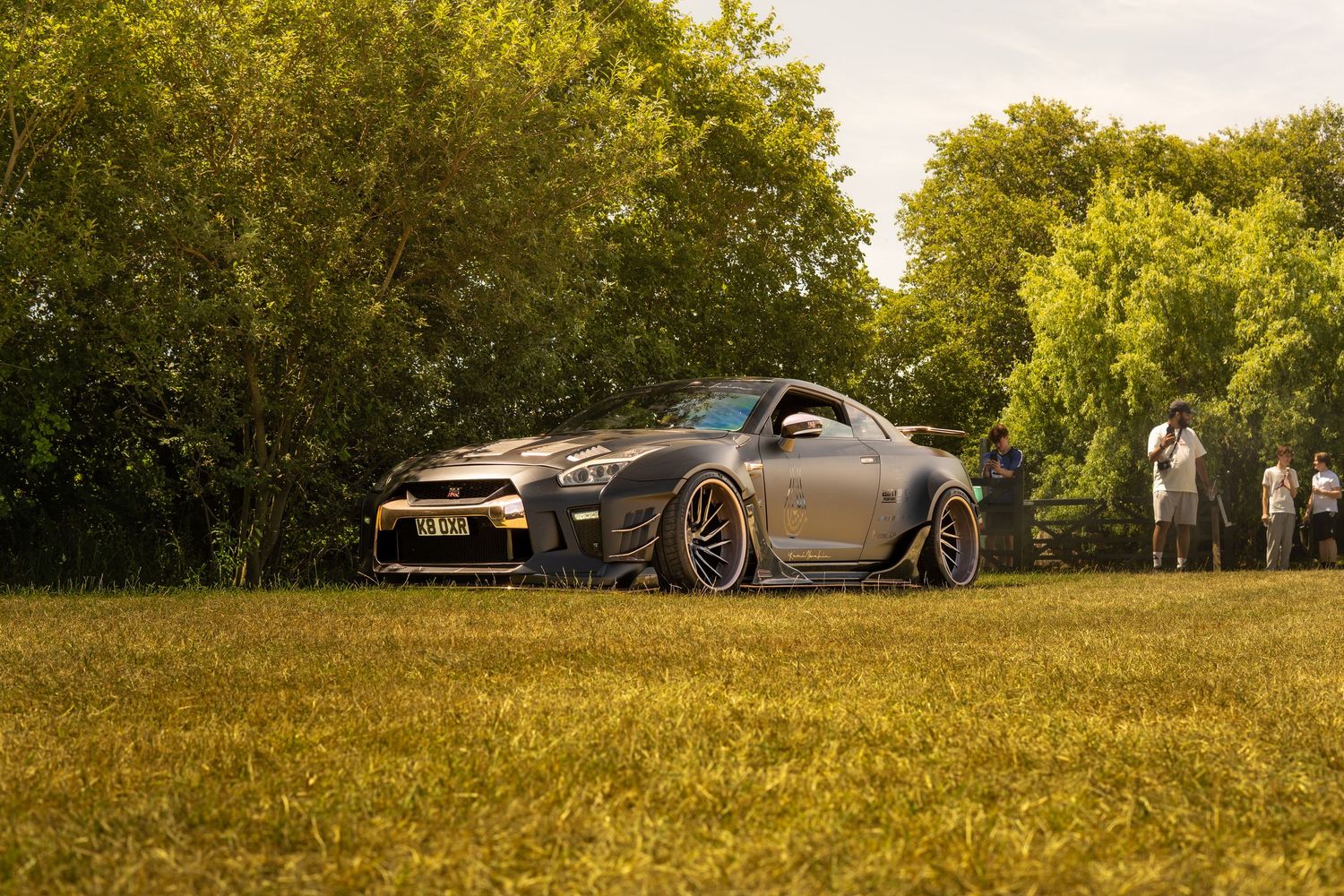 Modified Nissan GT-R with wide body kit parked on grass at a car meet.