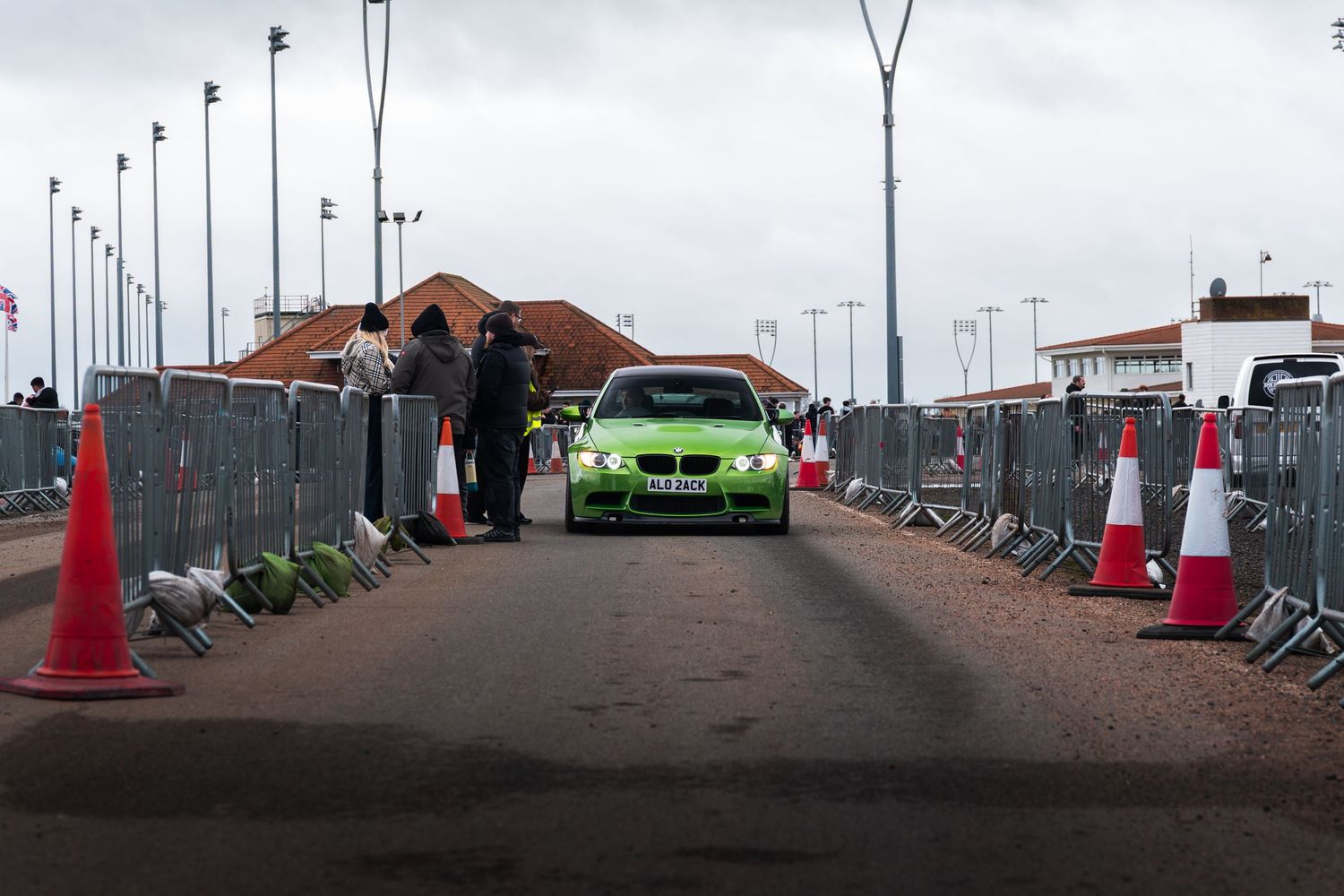 Bright green BMW driving through orange traffic cones at a UK car show entrance.