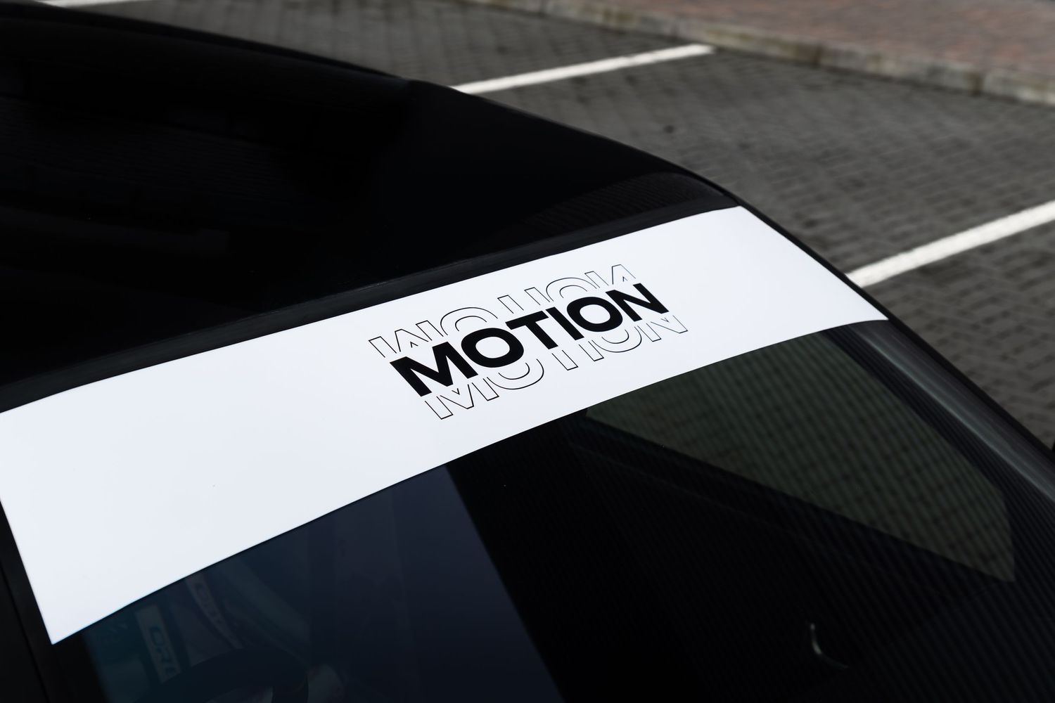 Close-up of Motion Automotive logo decal on black car windscreen banner strip.