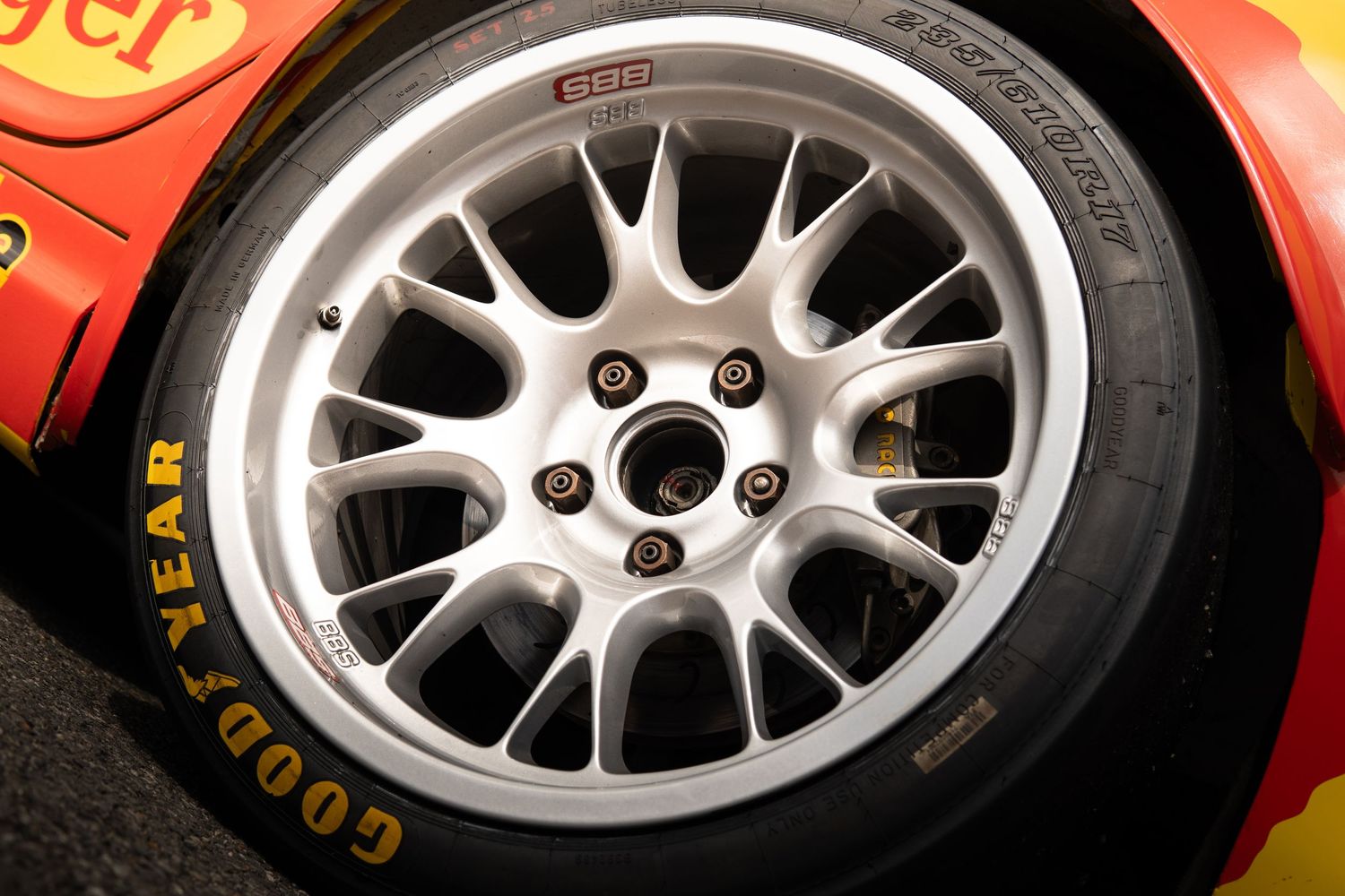 White multi-spoke alloy wheel with Goodyear tire on a red and yellow racing car.