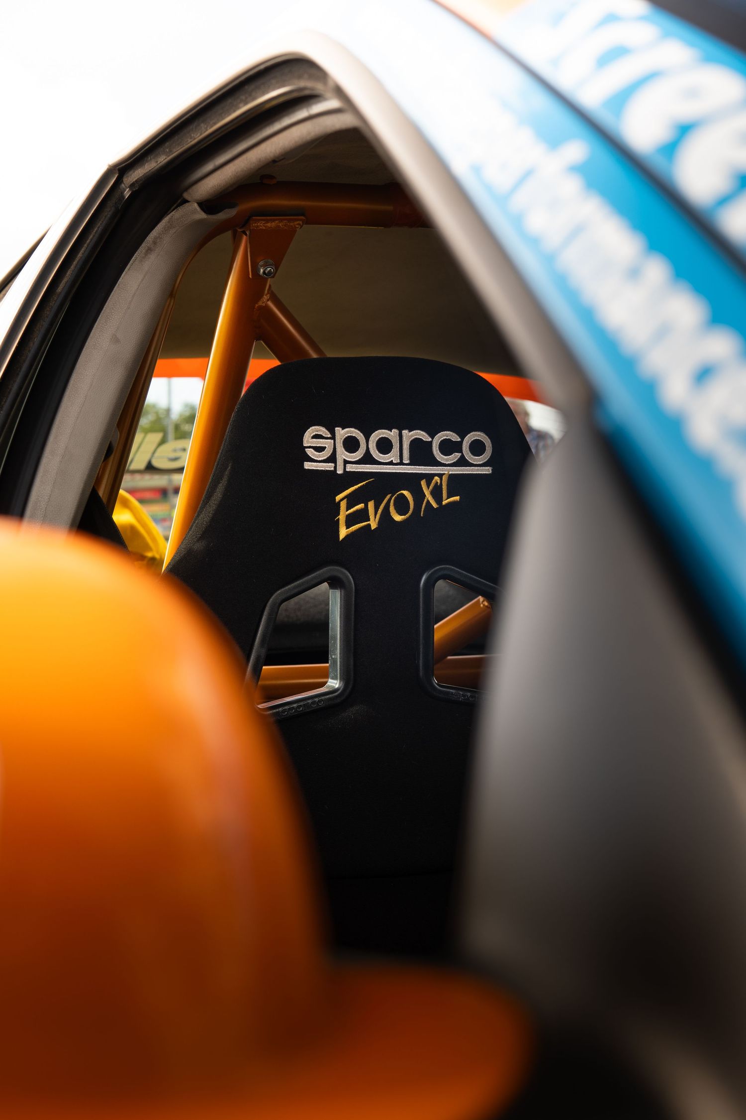 Sparco Evo XL black racing seat inside an orange and blue rally car with roll cage visible.