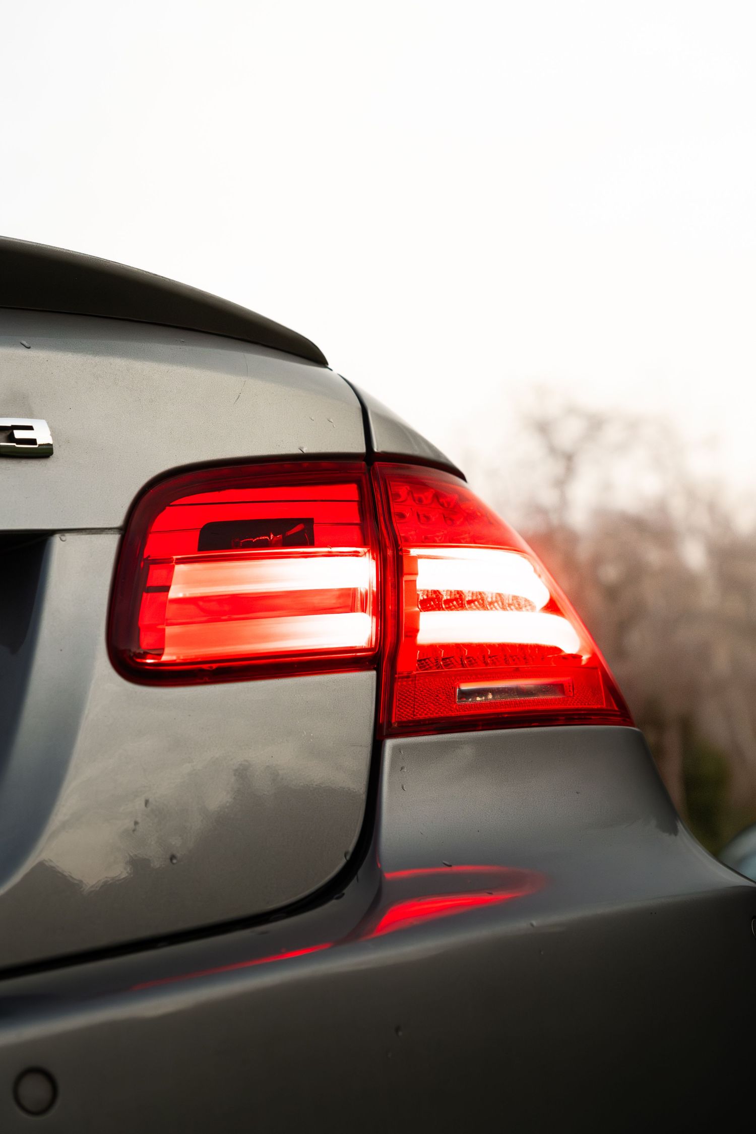 Close-up of illuminated red BMW tail light on a dark grey coupe in overcast conditions.