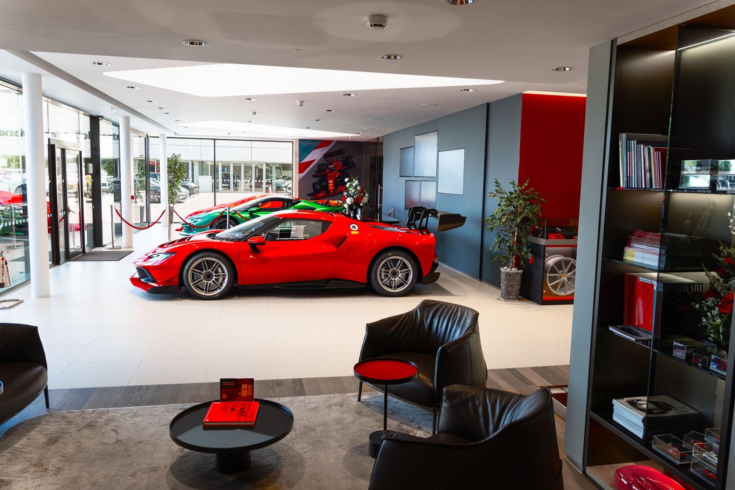 Red Ferrari on display in a luxury car dealership showroom with modern interior design and leather seating.