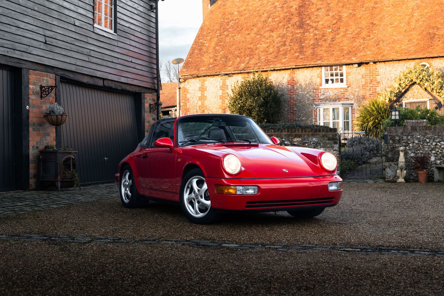 Classic red Porsche 911 964 Carrera photographed at dusk in front of a traditional English barn conversion.