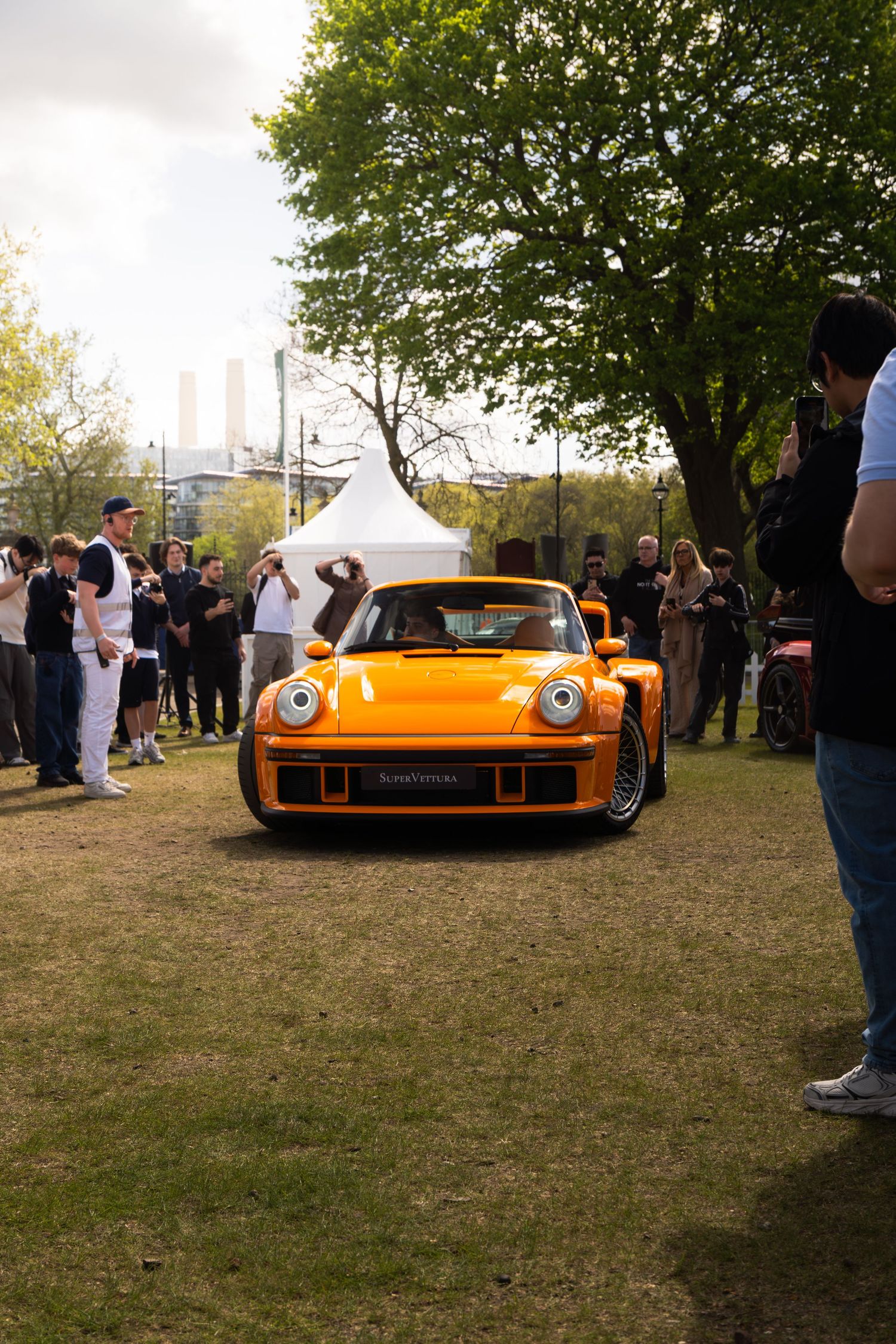 Front view of orange RWB Porsche 930 Turbo on grass with crowd at outdoor car show.
