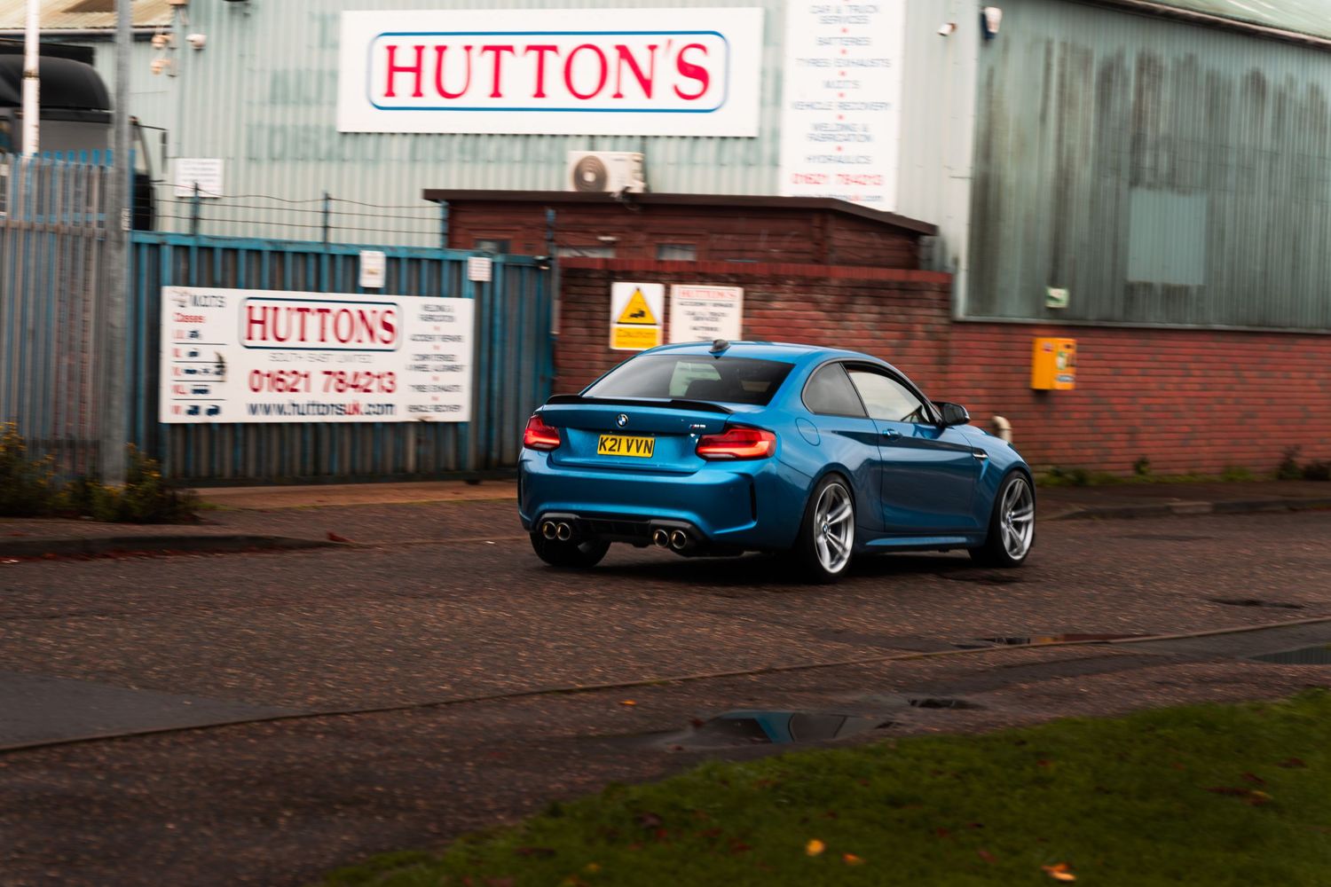 Blue BMW M2 coupe parked in lot outside Huttons industrial building.