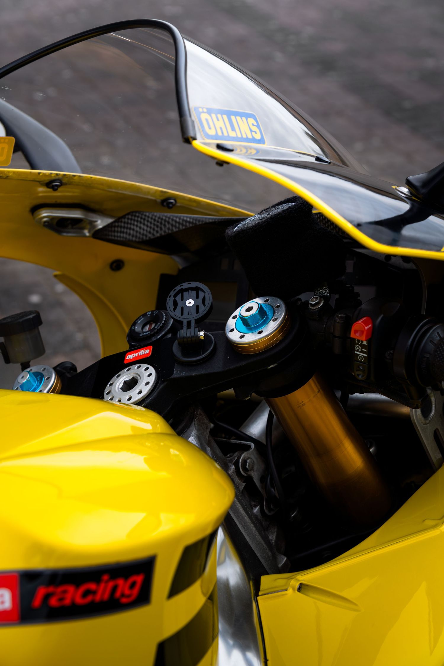 Cockpit view of yellow Aprilia RSV-R showing Ohlins windscreen, gold stem, and racing instrumentation.