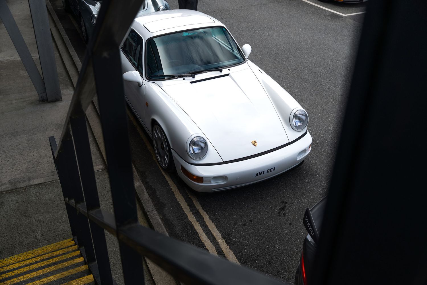 Aerial view of white Porsche 911 964 coupe in urban parking area.