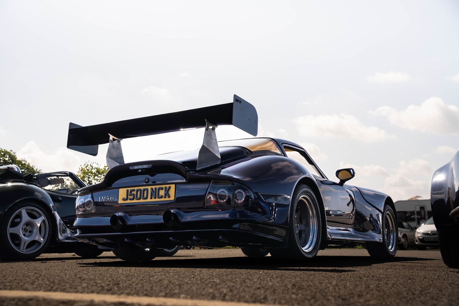 Dark blue Mosler MT900 supercar with large rear wing and J500 NCK number plate at a motorsport event.