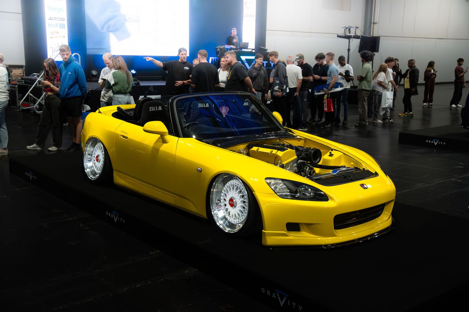 Yellow Honda S2000 convertible with BBS wheels and open hood on display at a car show.