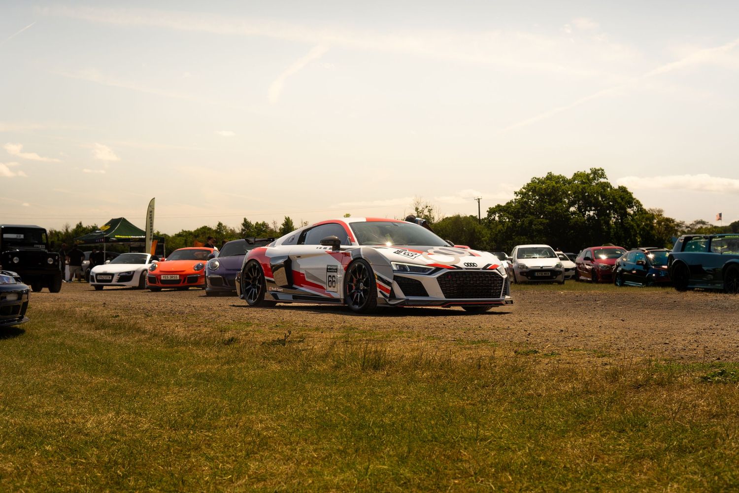 Audi R8 GT3 race car displayed at an outdoor automotive show with other exotic cars.